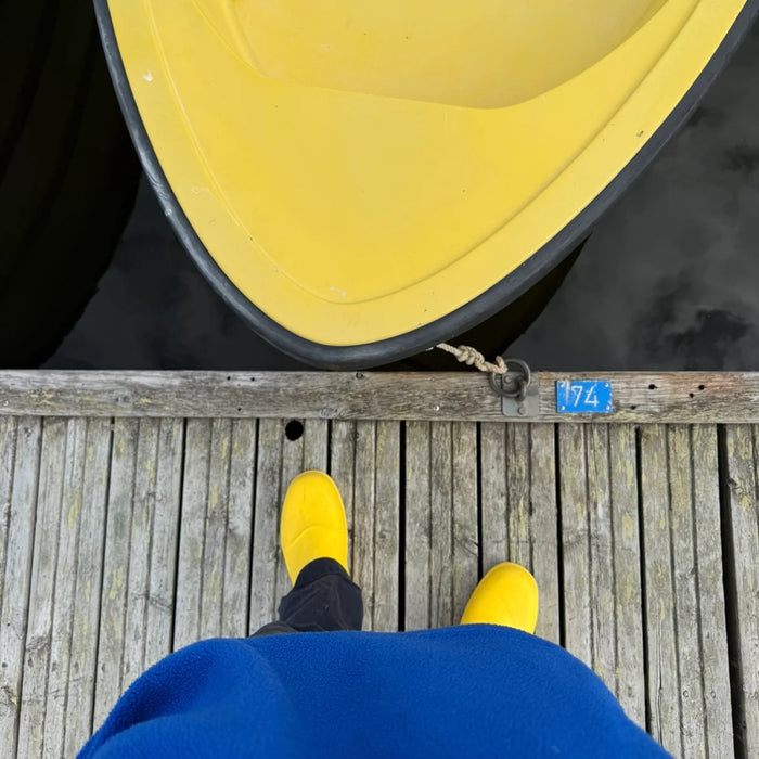 Gula Fubuki Nozawa-tofflor på en träbrygga bredvid en gul båt, sedda uppifrån